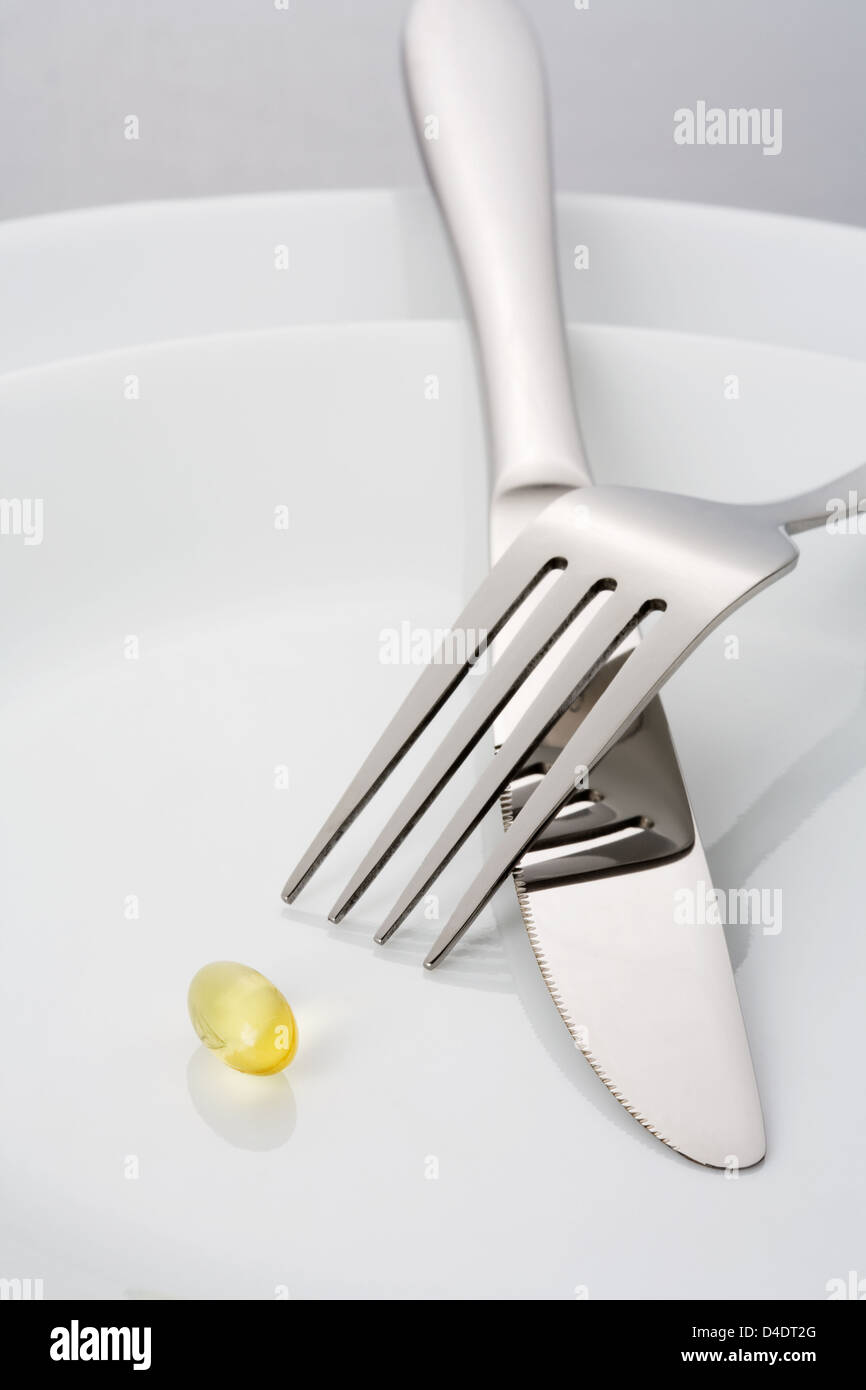Fork, knife and a single fish oil capsule on a plate Stock Photo