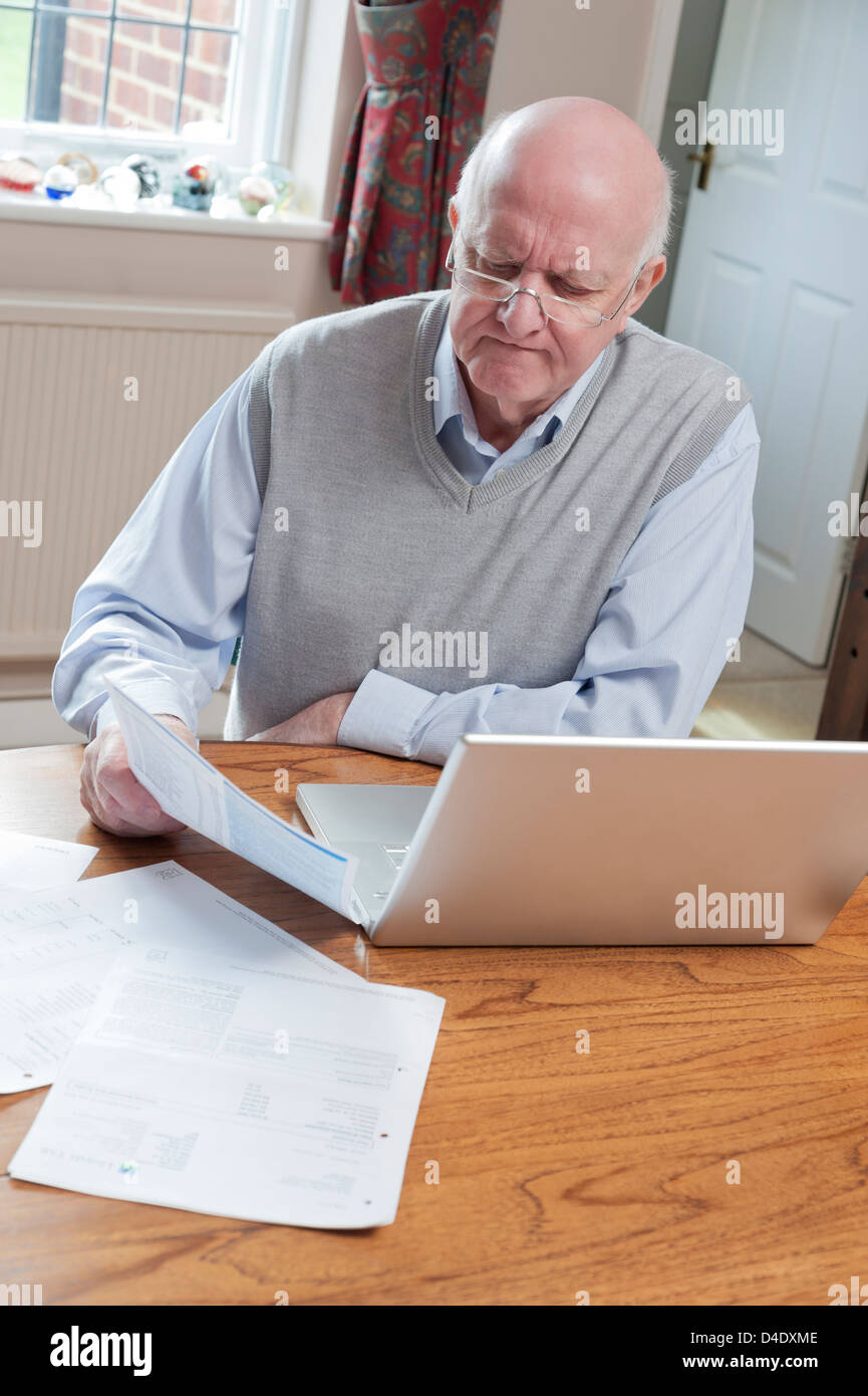 Senior man looking at bills at home with laptop Stock Photo
