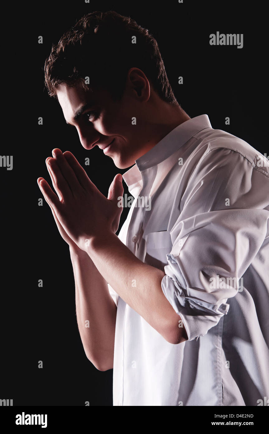 Young man praying in darkness with an enigmatic smile Stock Photo