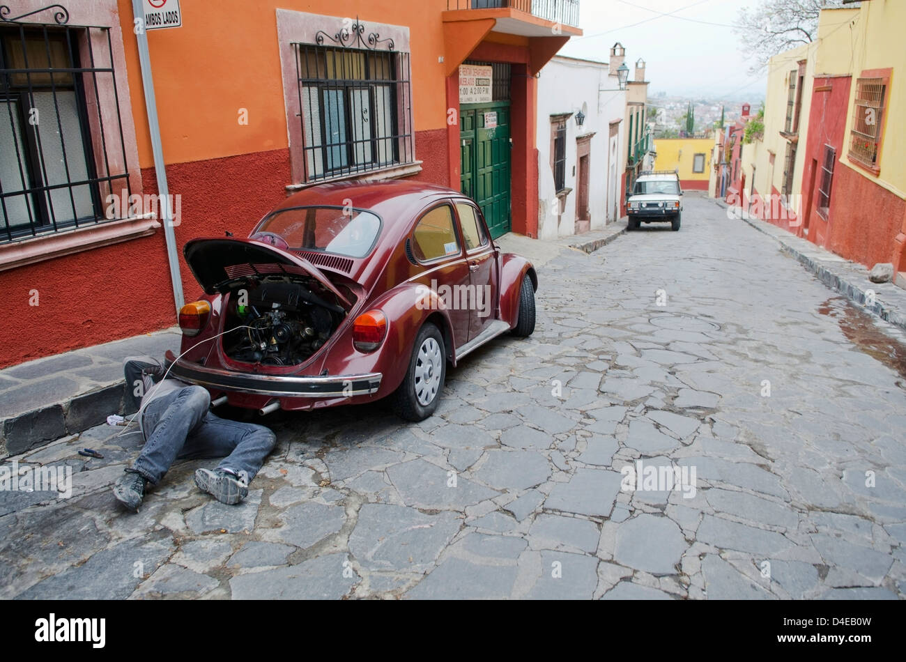 Man repairing volkswagen beetle parked on cobblestone street; San Miguel de Allende, Guanajuato, Mexico Stock Photo