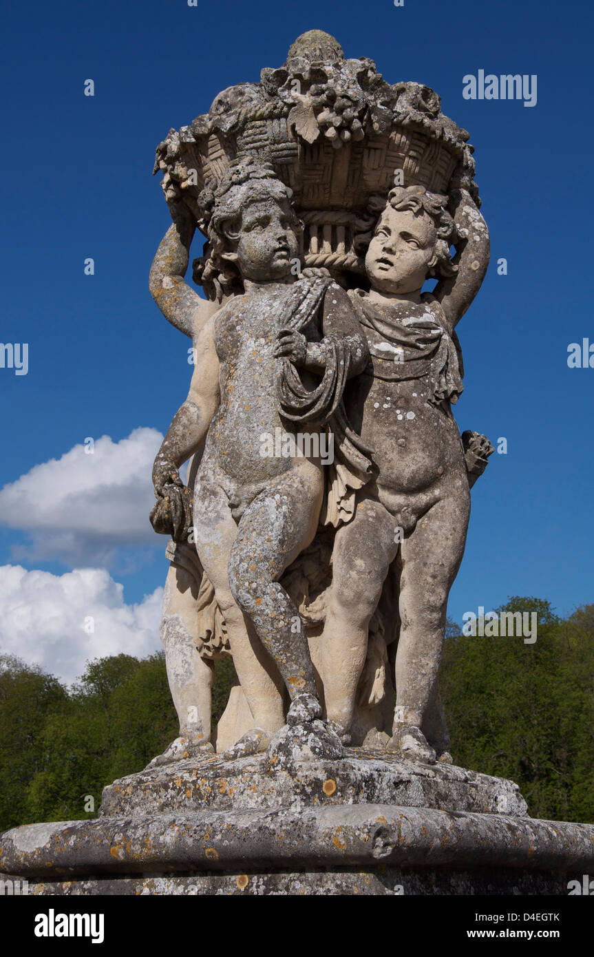 An ornamental statue of cherubic infants holding up a basket of flowers and fruit, in the gardens of the baroque Château of Vaux-le-Vicomte. France. Stock Photo