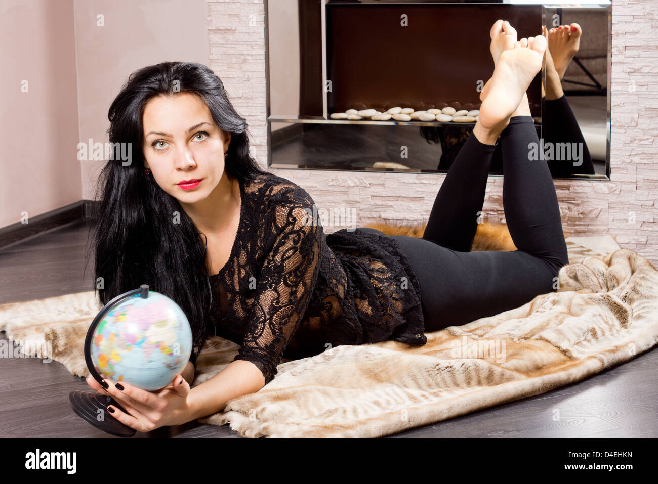 Beautiful woman planning a trip lying barefoot on a fur coat on the floor clutching a globe in her hands Stock Photo
