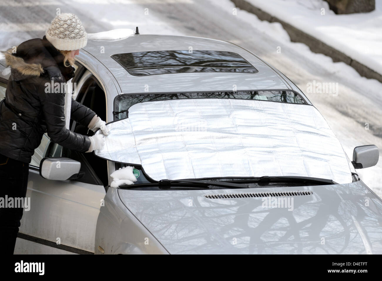 A woman places a antifreeze tarpaulin onto the windshield of a car
