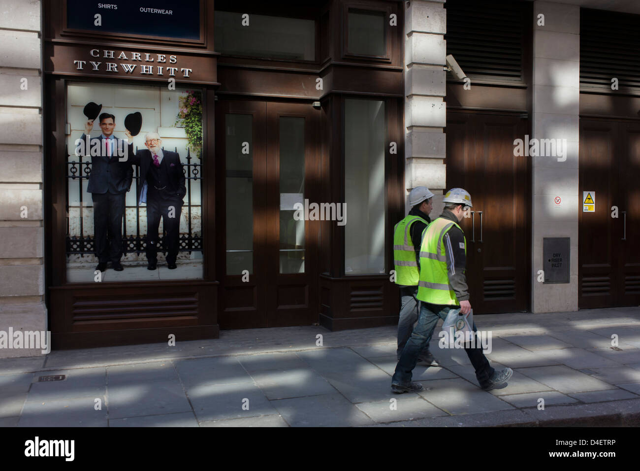 Two manual labourers walk past the Charles Tyrwhitt menswear outfitters at Liverpool Street in the City of London, the capital's heart of its financial district - a good location for suits and businesswear. A pair of Englishmen raise their bowler hats in a gesture from a previous era, when hats said much of your social standing, a summary of your position in the class system. In the 21st century though, the hat is largely an item of clothing to wear only for extreme cold or heat. Stock Photo