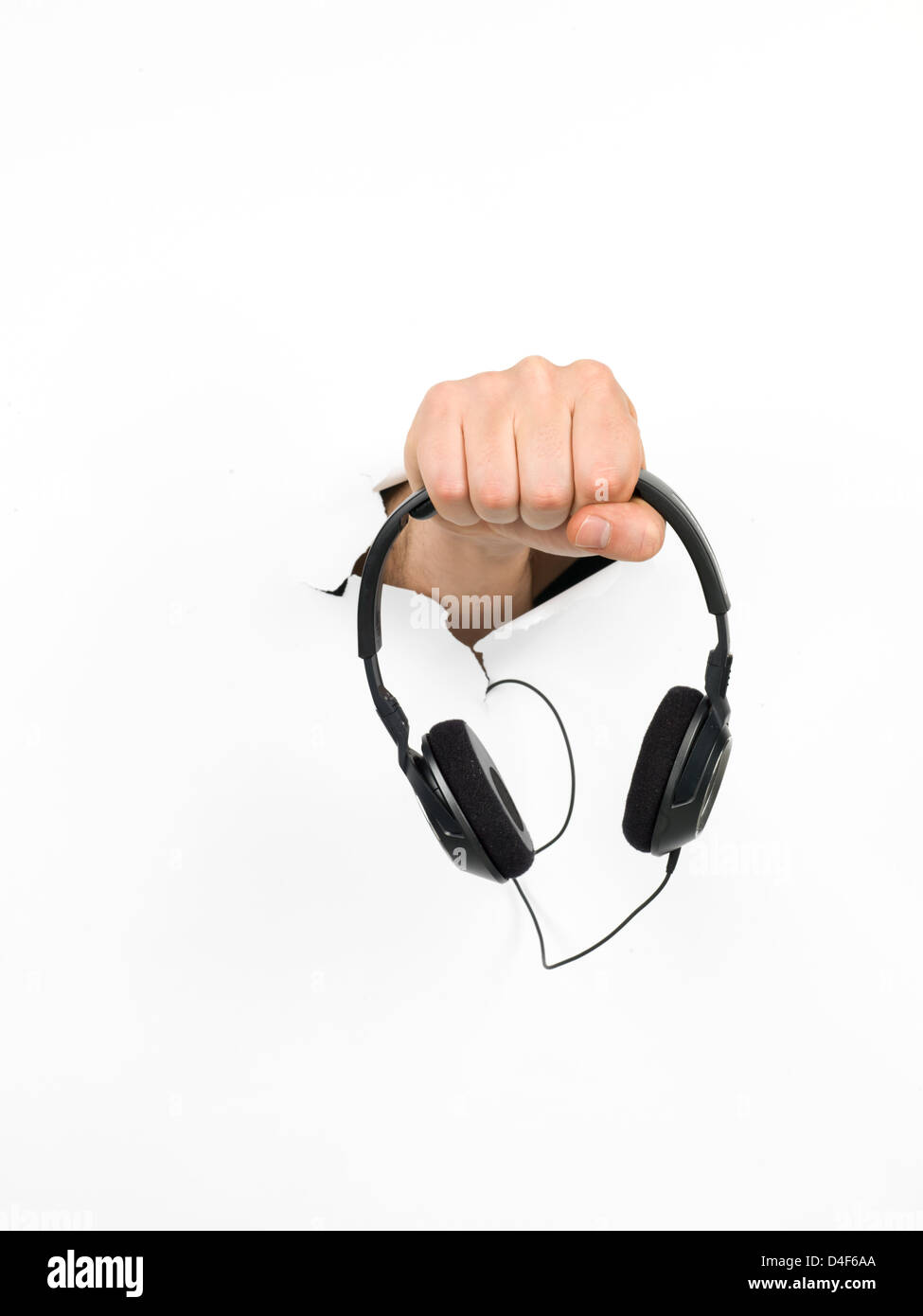 close-up of male hand holding a pair of black headphones through a hole in a white paper, isolated Stock Photo