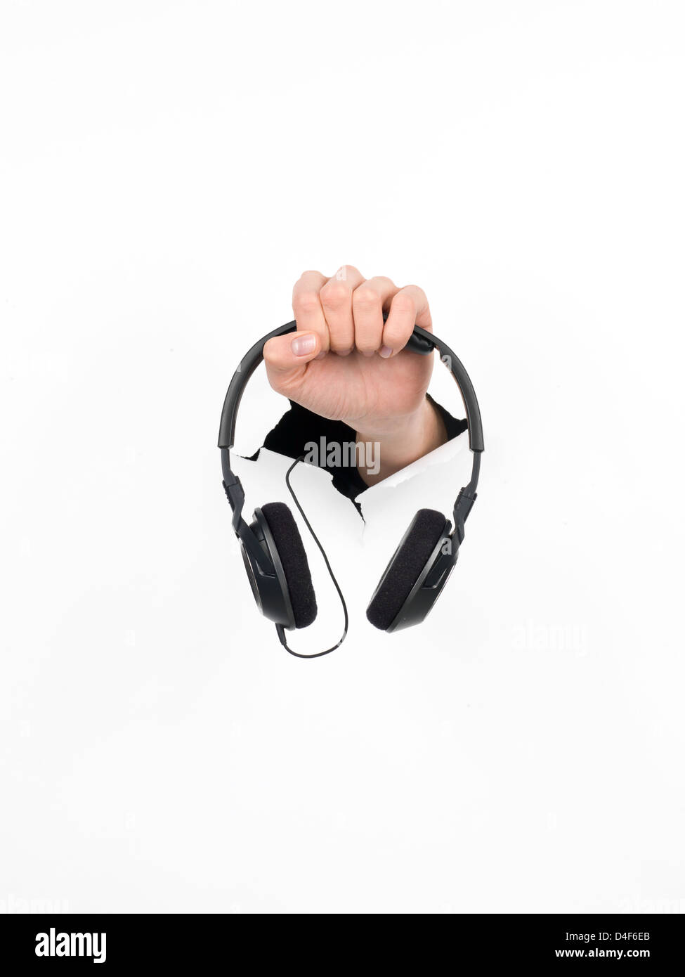 close-up of female hand holding a pair of black headphones through a hole in a white paper, isolated Stock Photo