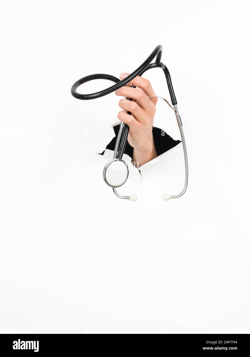 close-up of female hand holding a stethoscope through a torn white paper, isolated Stock Photo