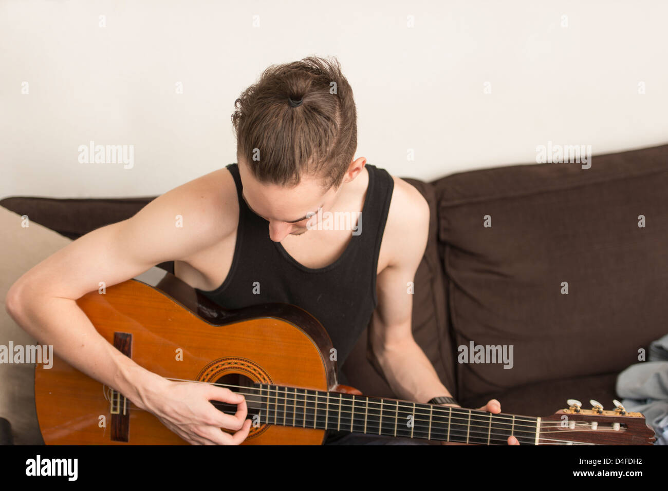 Young adult male sit in sofa and practice on his acoustic guitar Stock Photo