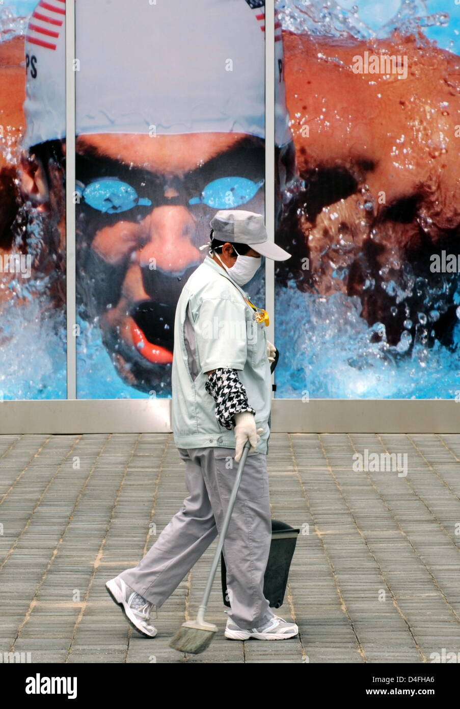 A sweeper with a pollution mask passes an advertising picture of US swimmer Michael Phelps prior to the 2008 Olympic Games, Beijing, China, 07 August 2008. Photo: Bernd Thissen ###dpa### Stock Photo