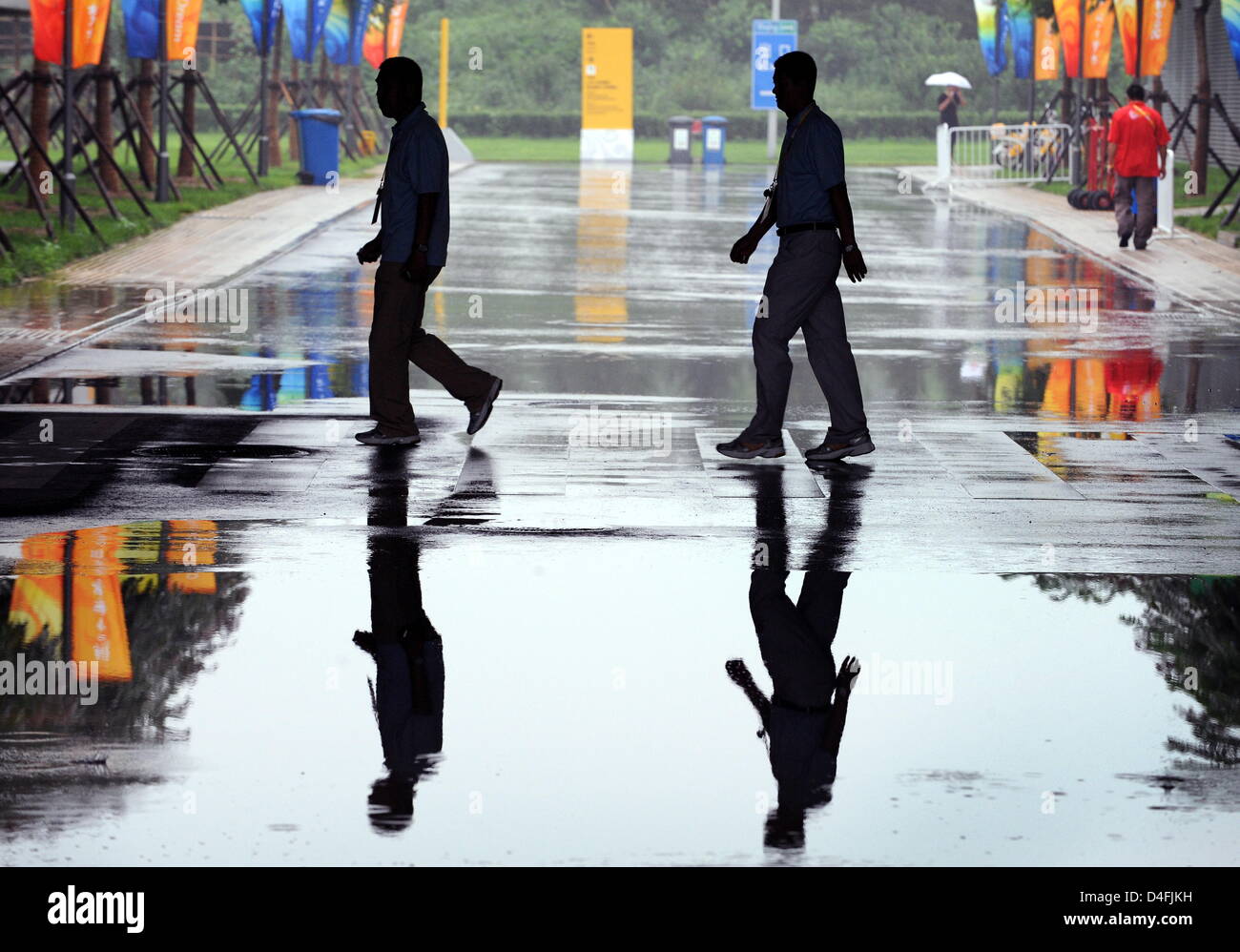 The shadows of officials crossing a street are reflected in a puddle at the Olympic Green Tennis Center during a rain delay in Beijing during the Beijing 2008 Olympic Games at the National Aquatics Center in Beijing, China 10 August 2008. The 1st round match mens single tennis match of Nicolas Kiefer from Germany and Max Mirnyi from Belarus is unhold because of heavy rain. Photo: K Stock Photo