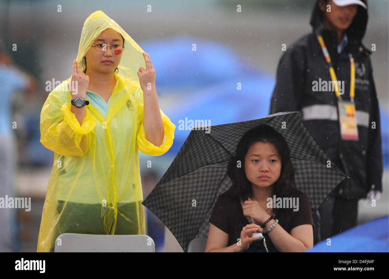 Spectators standing in the rain at the Olympic Green Tennis Center during a rain delay at the Beijing 2008 Olympic Games at the National Aquatics Center in Beijing, China 10 August 2008. The 1st round match mens single tennis match of Nicolas Kiefer from Germany and Max Mirnyi from Belarus is unhold because of heavy rain. Photo: Karl-Josef Hildenbrand dpa ###dpa### Stock Photo