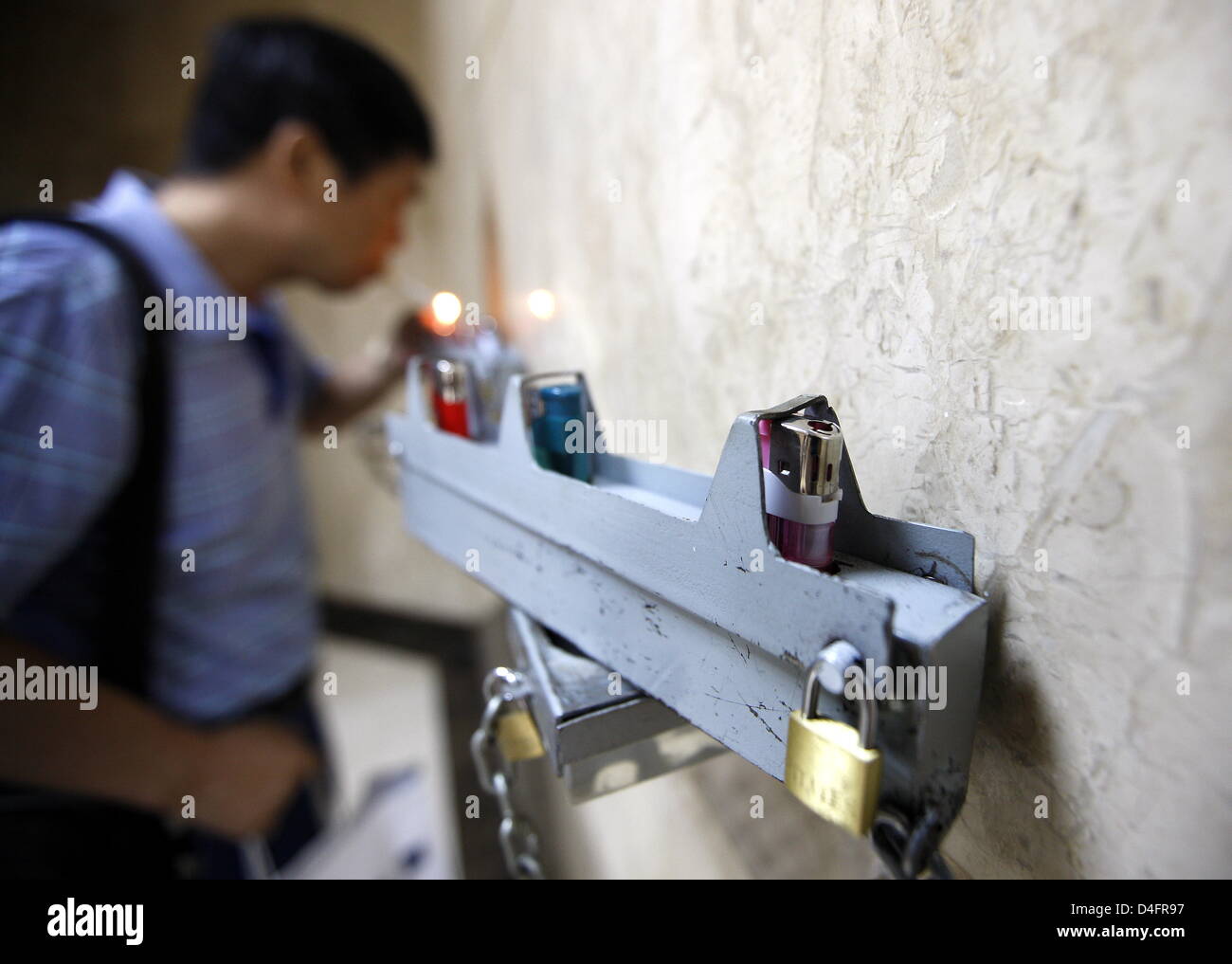 A Chinese lights a cigarette with a lighter that's attached to a wall