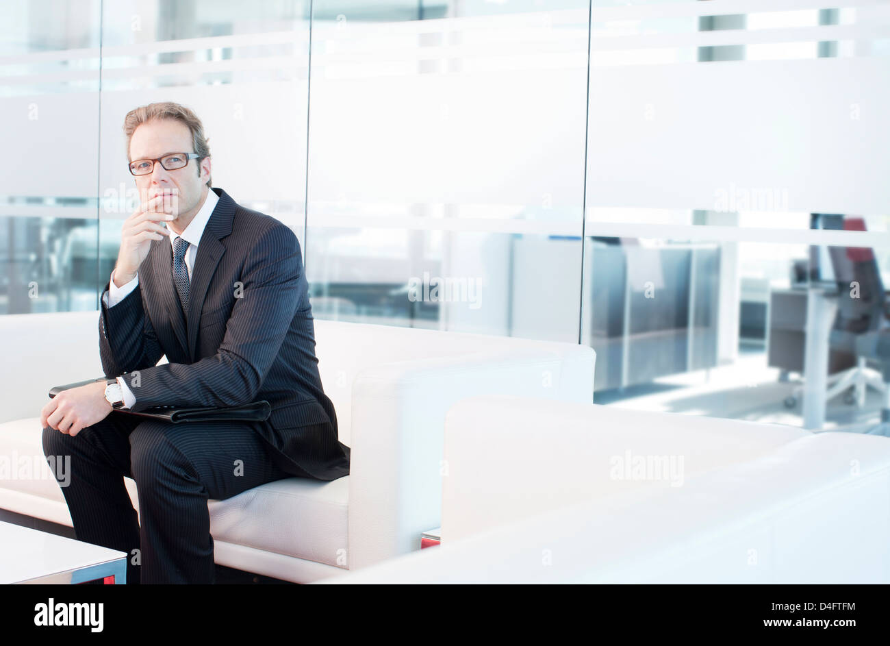 Businessman sitting on sofa in office lobby Stock Photo