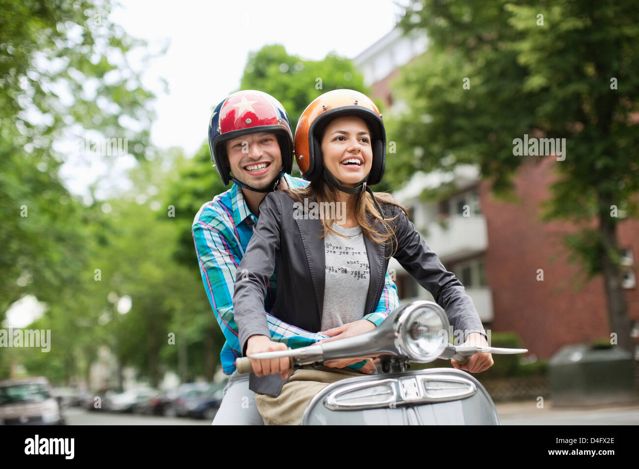 Couple riding scooter together on city street Stock Photo