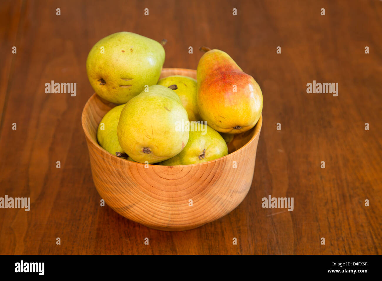 A hand made wood bowl on a wood table full of fresh, bartlett pears Stock Photo