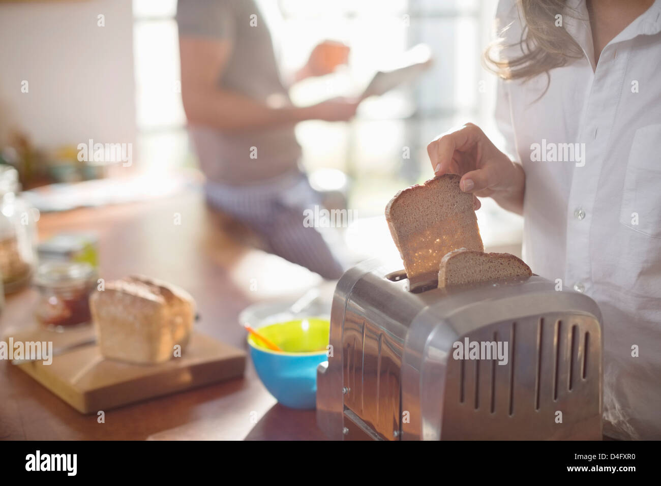 Woman putting bread in toaster Stock Photo