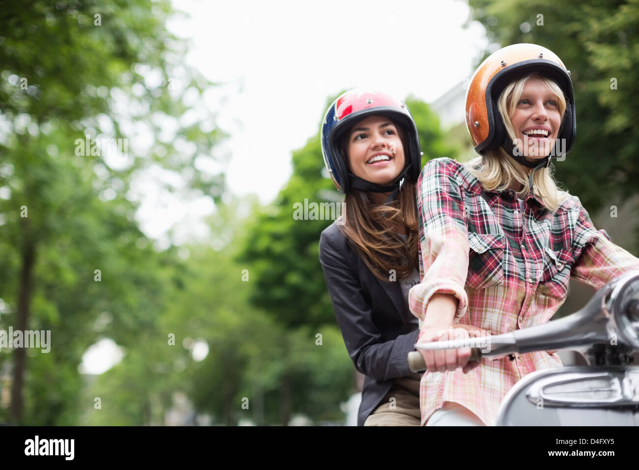 Women riding on scooter together outdoors Stock Photo