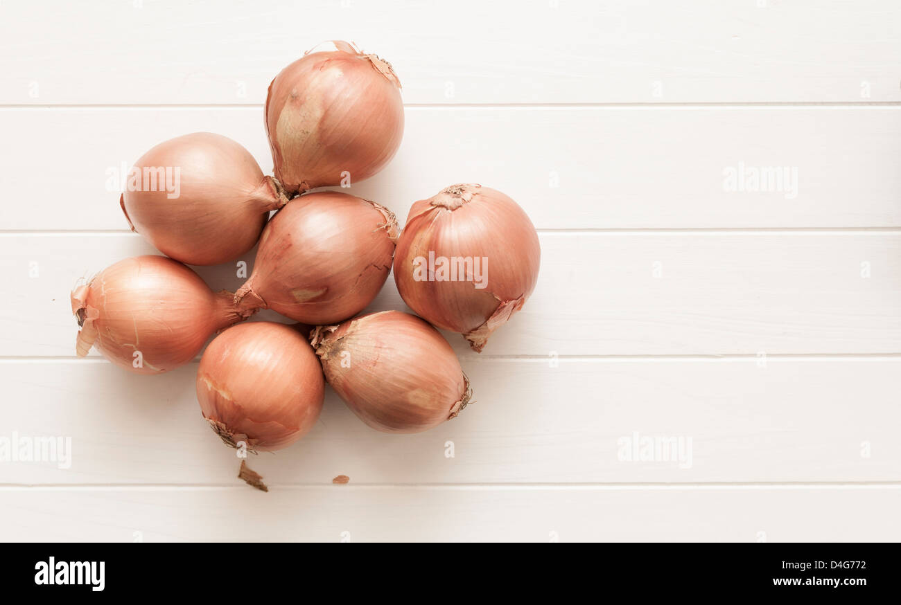 Onions with skins on, on a white table. Stock Photo