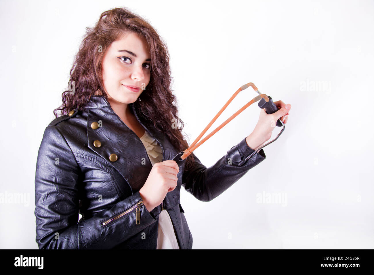 brunette young girl holding a slingshot aiming at the camera smiling Stock Photo