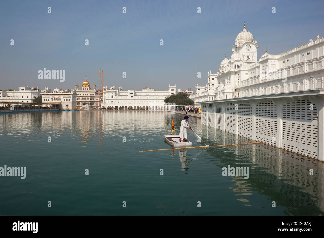 Sikh man cleaning the Holy Pool from a small boat at the Golden Temple ...