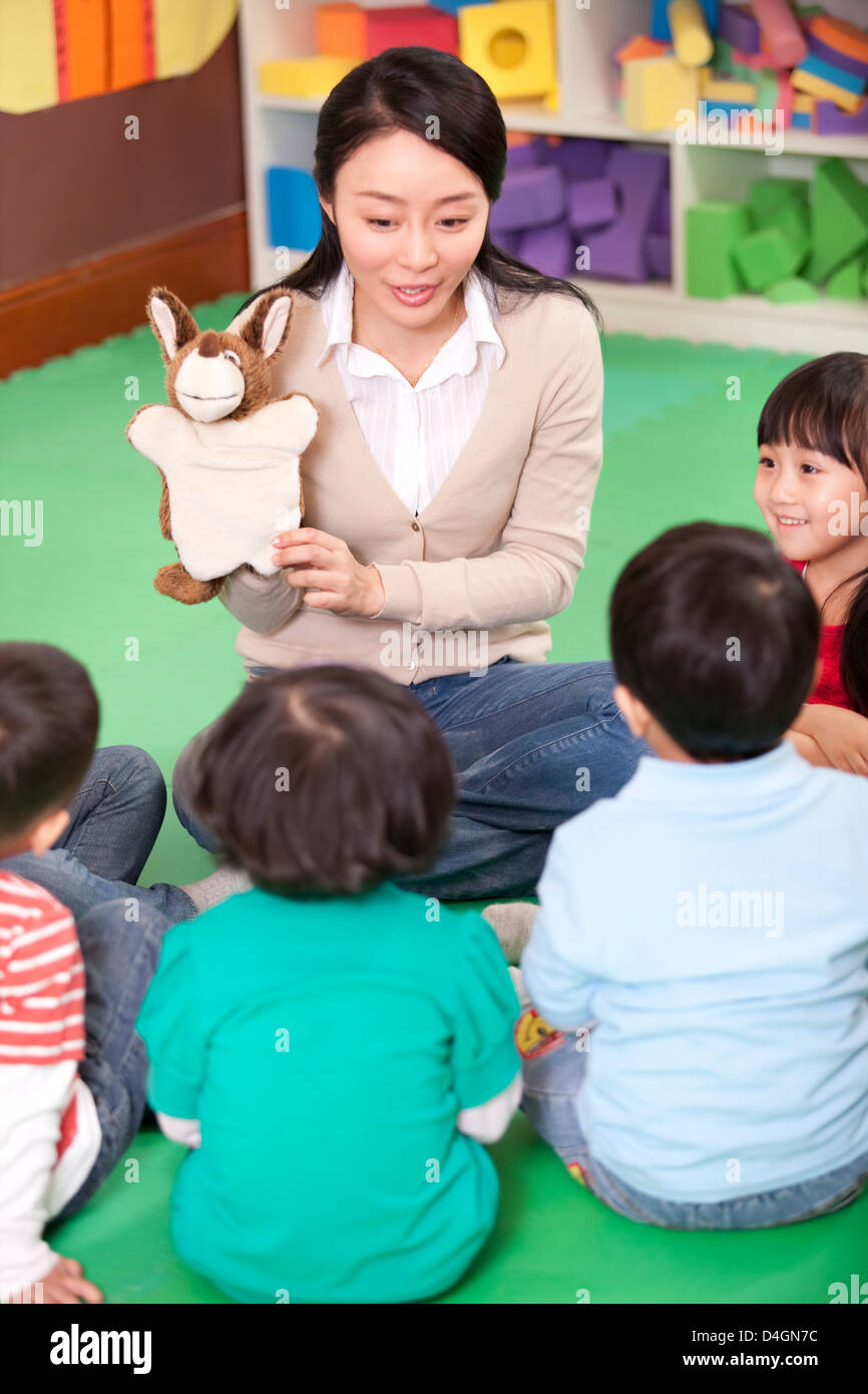 Female teacher playing hand puppet game with cute kindergarten children