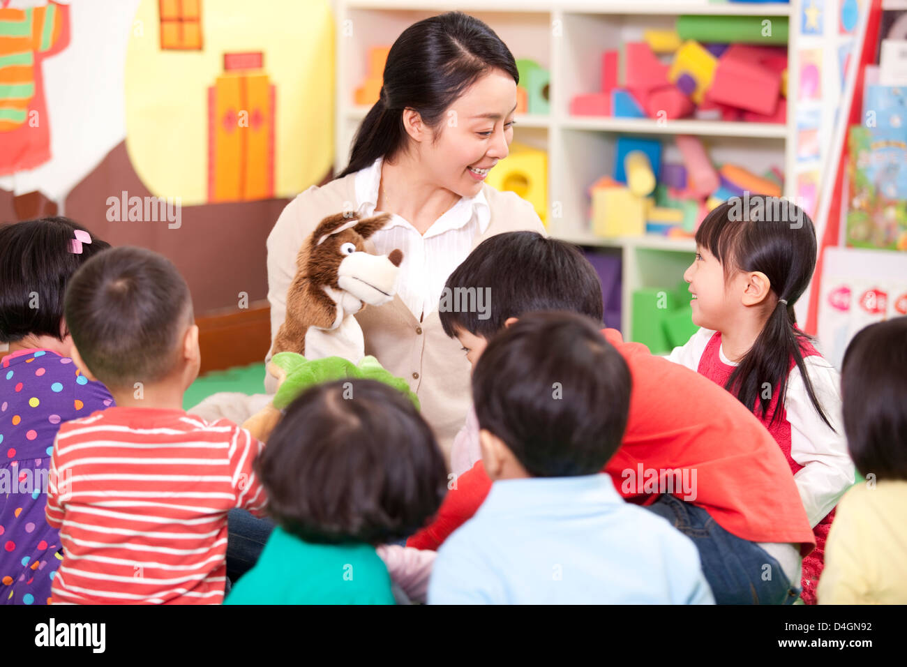 Female teacher playing hand puppet game with cute kindergarten children