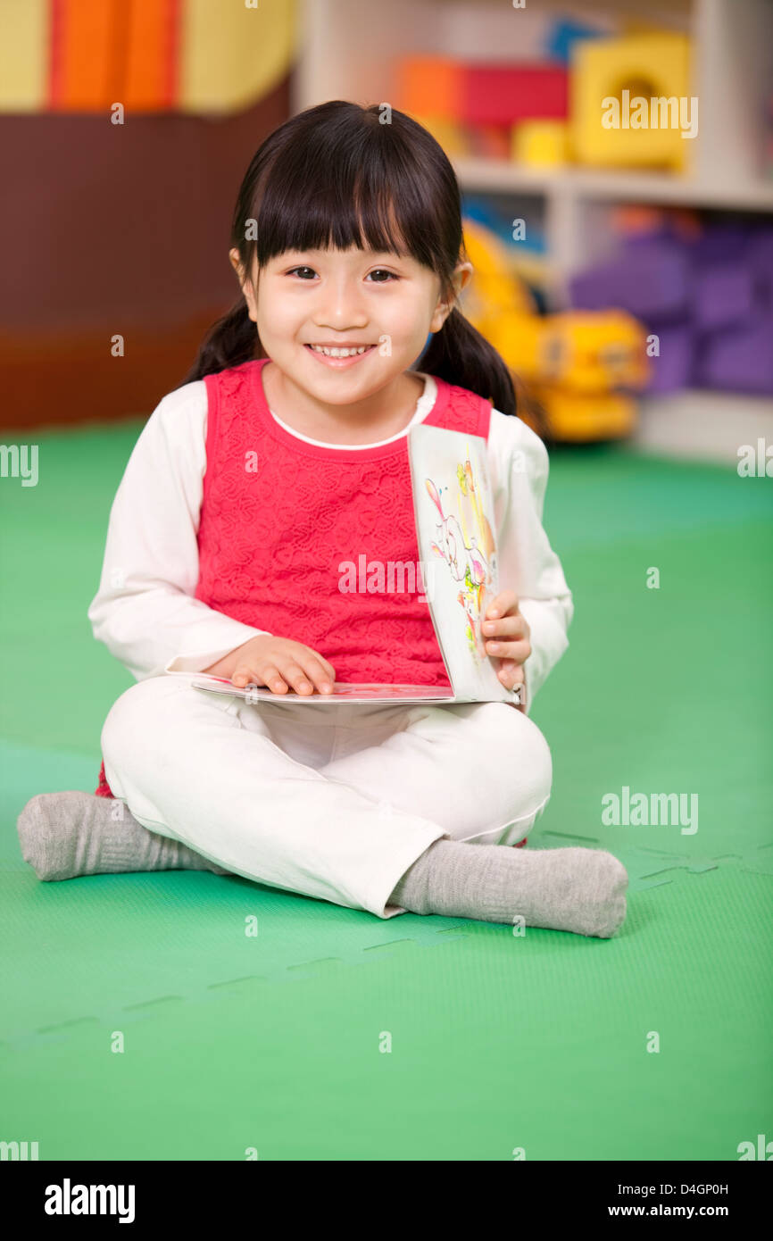 Cute little girl sitting on floor with book in hand Stock Photo - Alamy