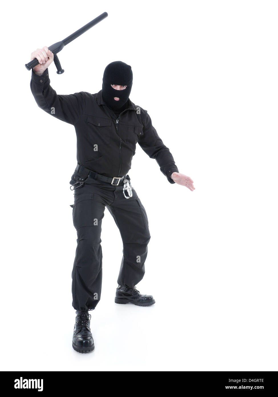 Anti-terrorist police guy wearing black uniform and black mask holding firmly police club in one hand raised in the air Stock Photo