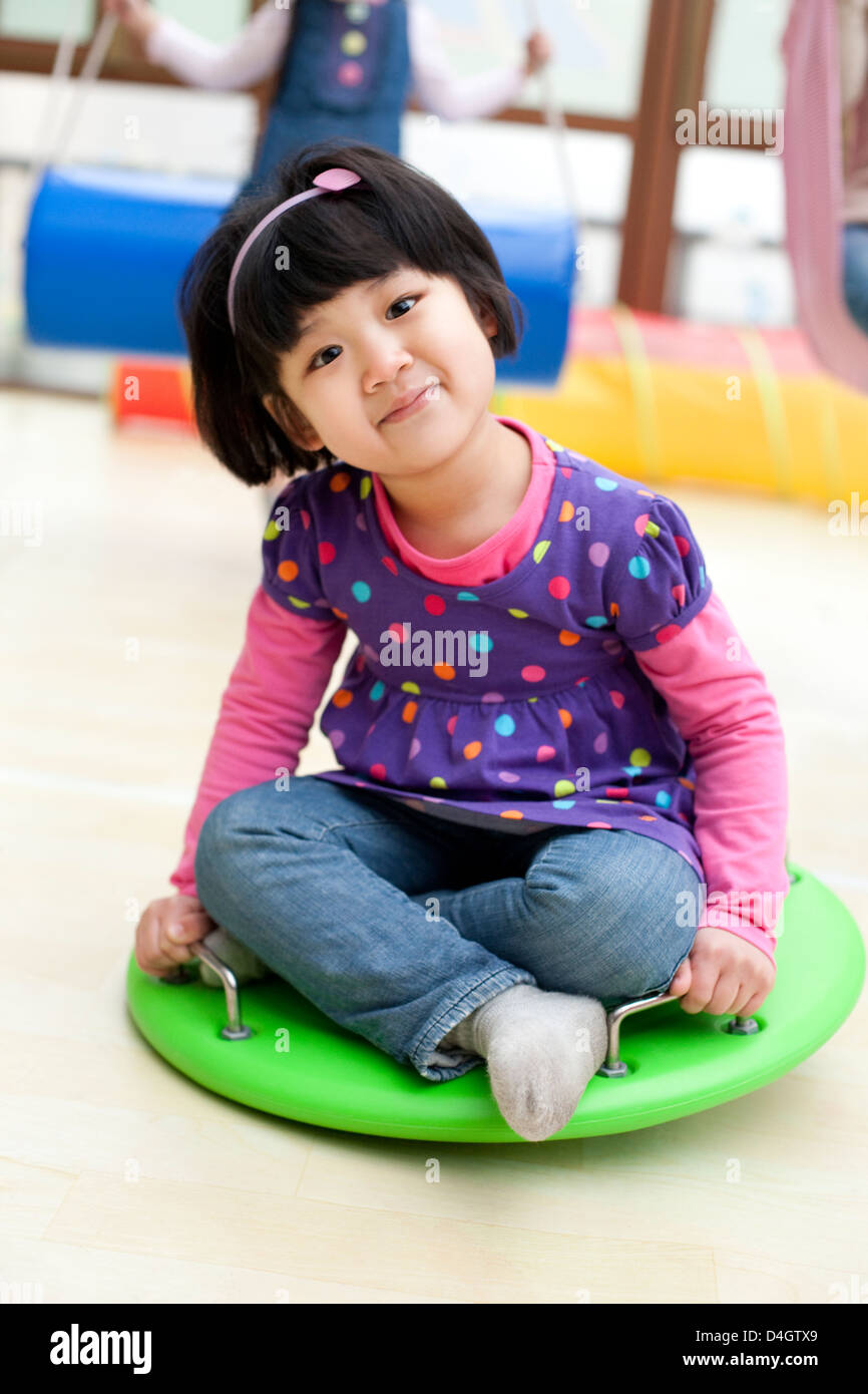 Cute girl sitting on a big toy dreidel in kindergarten Stock Photo