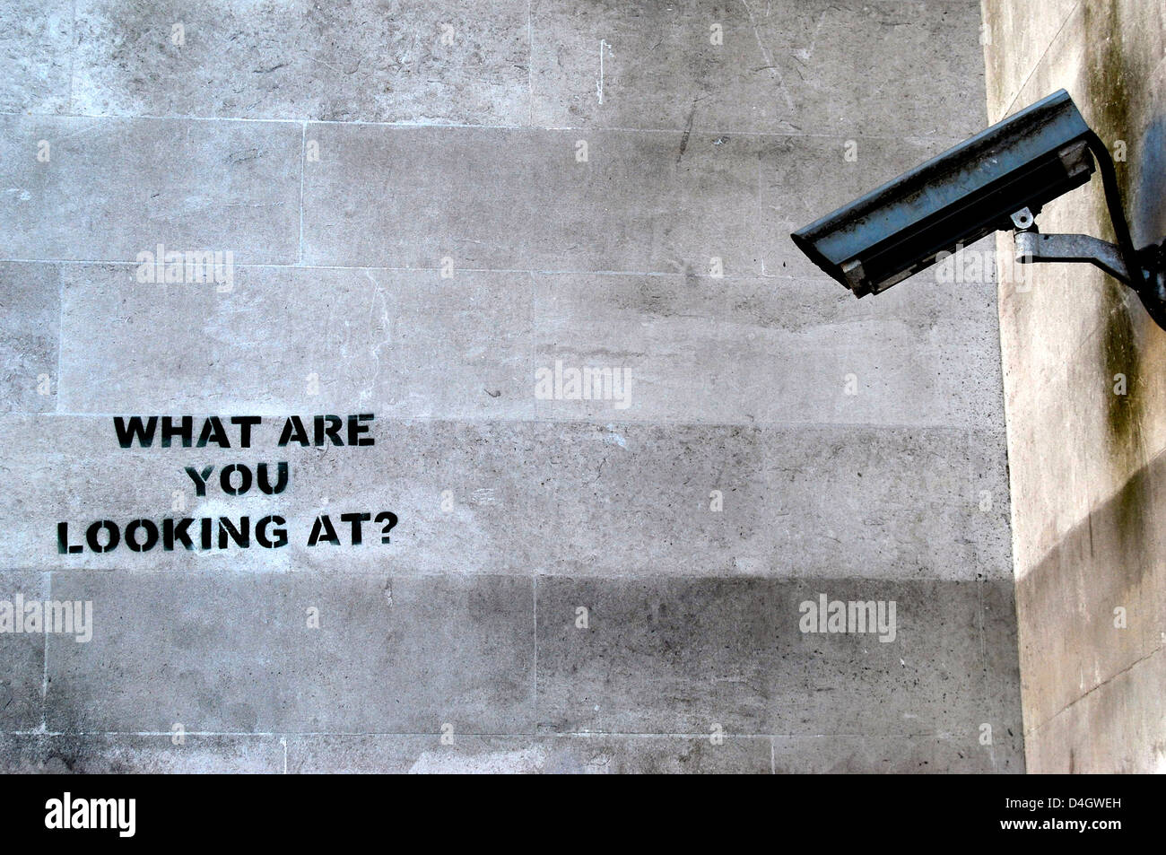 A mural by Banksy reads 'what are you looking at' next to a CCTV camera. Stock Photo
