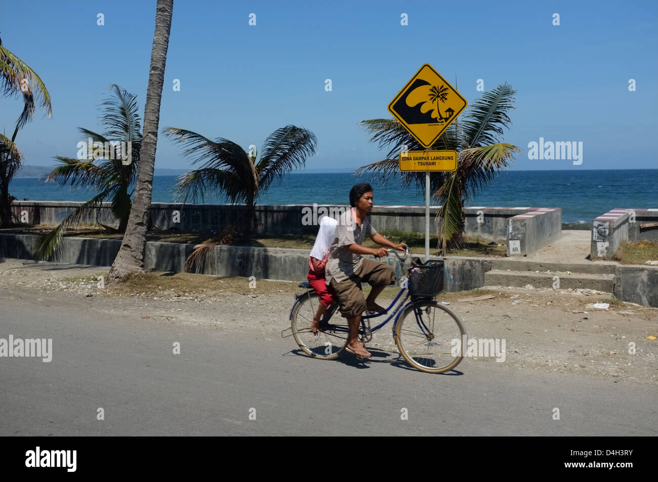 Boy cycling past a tsunami warning sign in Pangandaran, West Java, Indonesia Stock Photo