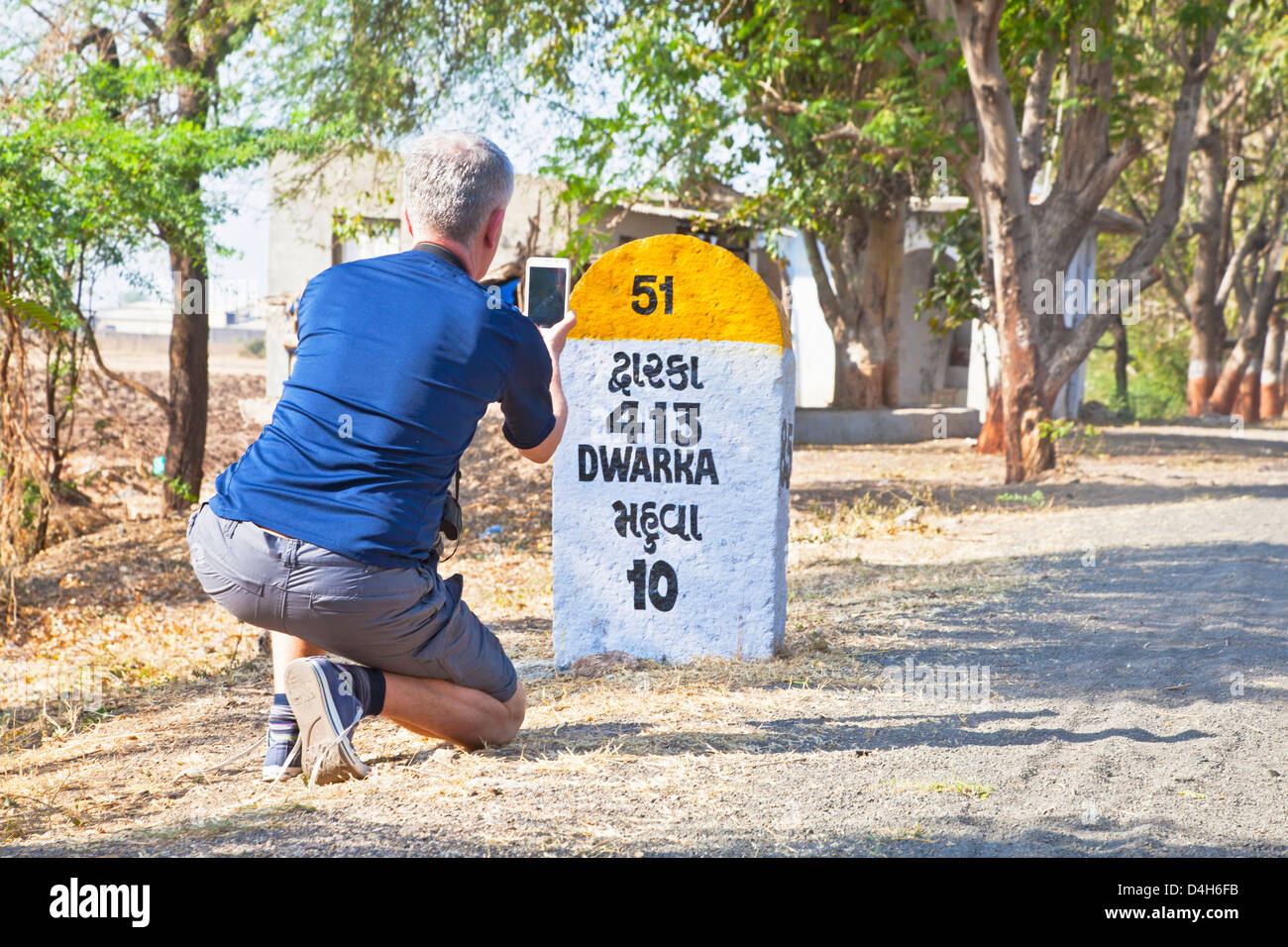 Caucasian male taking a photo of the 413km milestone to Dwarka passing through Mahuva Gujarat India Stock Photo