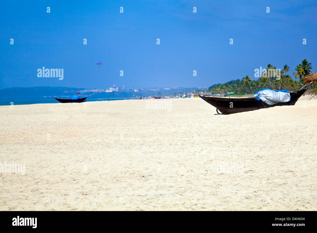 Landscape of generic beach with white sand, blue sky, sea, surf, para gliders and fishing boats for a backdrop Stock Photo