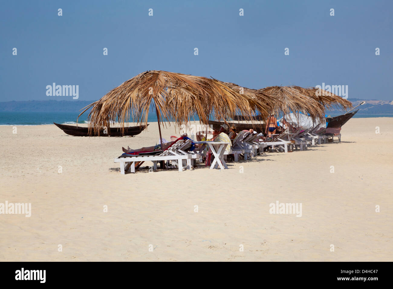Landscape of tropical beach scene in Goa India with sunbathers taking shelter from the hot mid day sun on loungers chilling Stock Photo