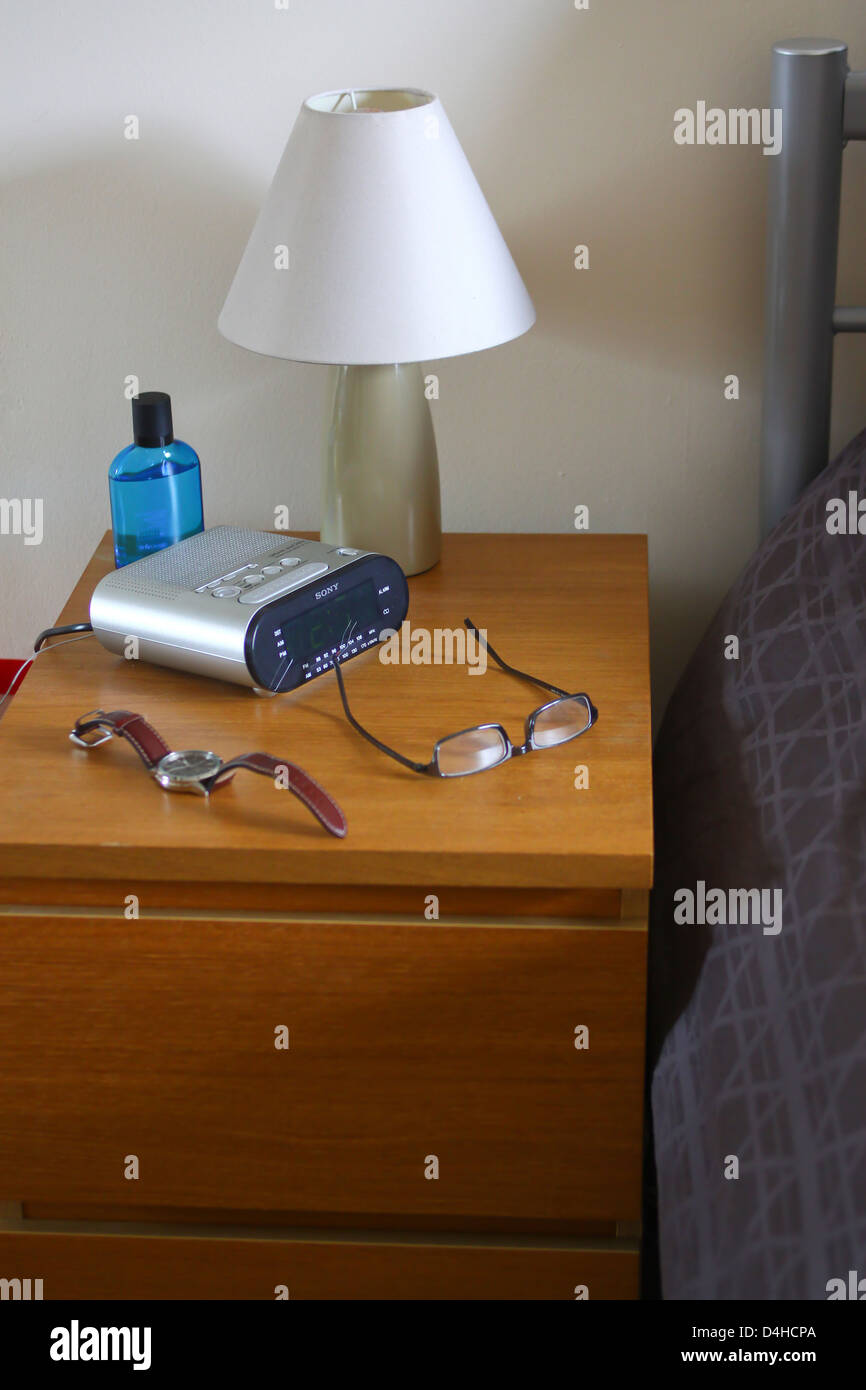 Bedside table with lamp clock radio watch and specs Stock Photo