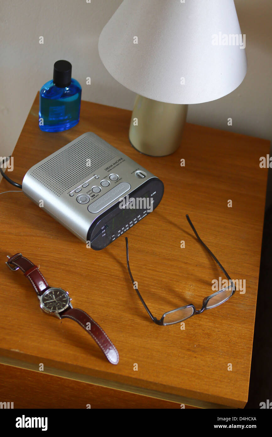 Bedside table with lamp clock radio watch and specs Stock Photo