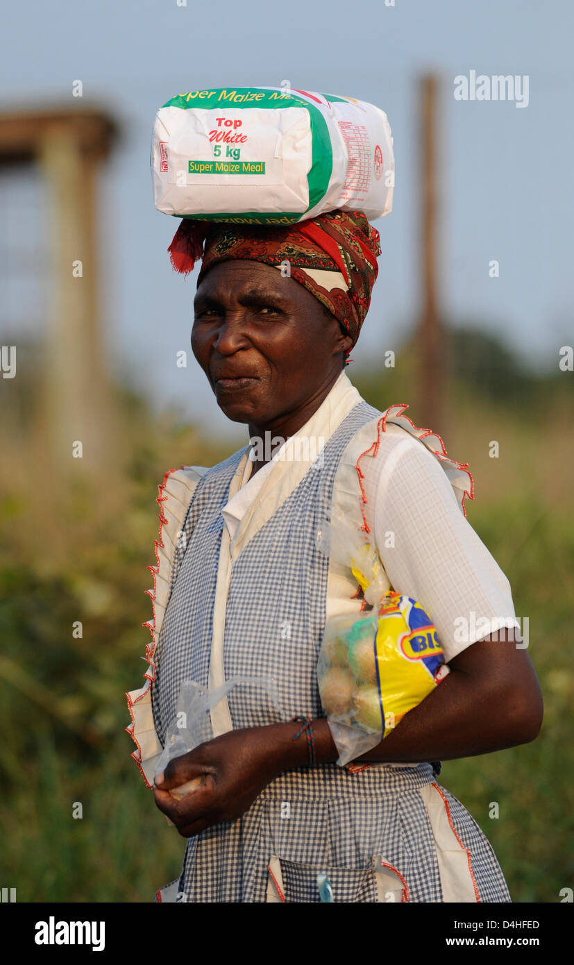 An elderly SouthAfrican woman balances a large packet of meal on her