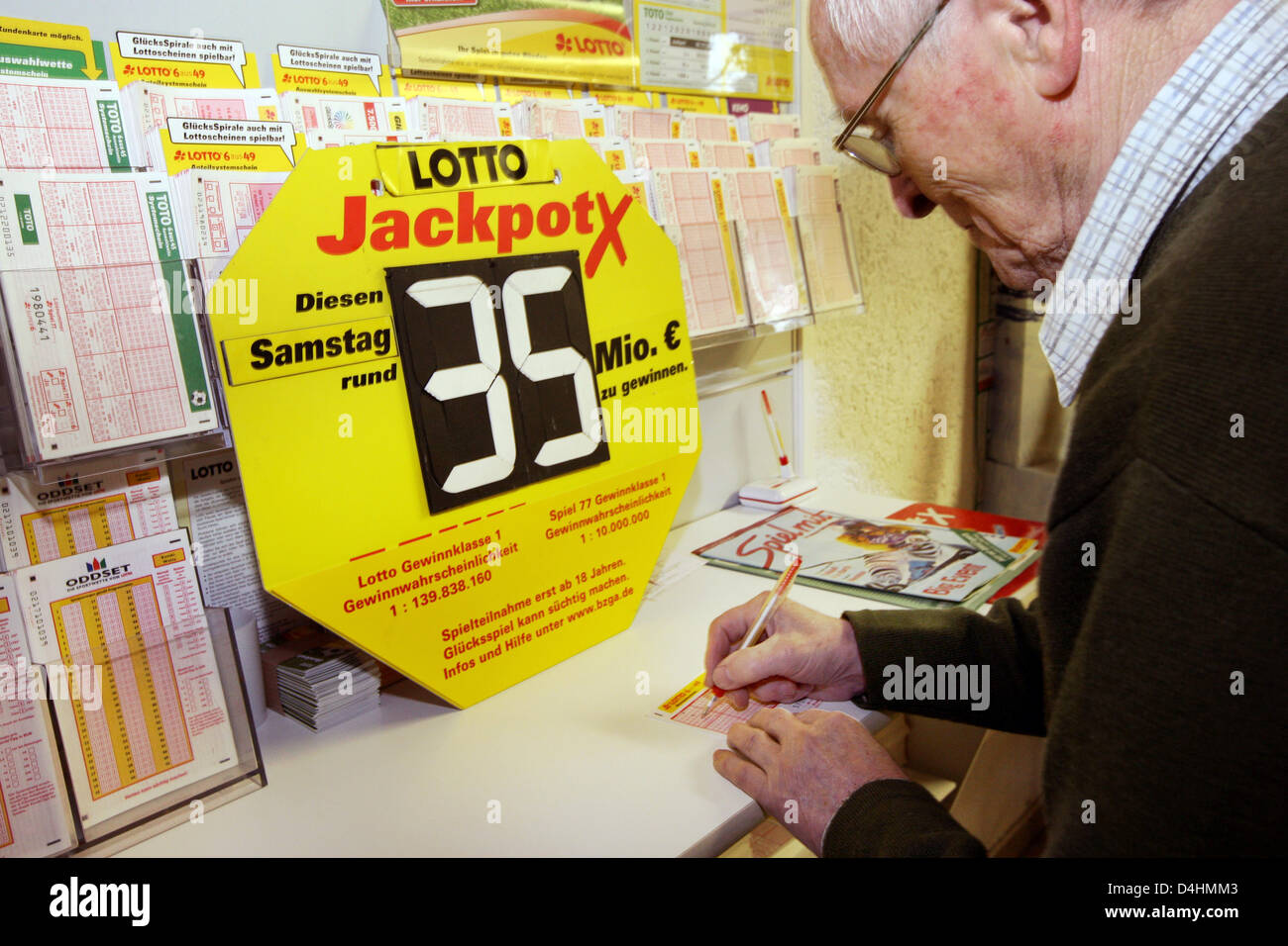 A man fills in his lottory ticket in front of a sign advertising the latest  German