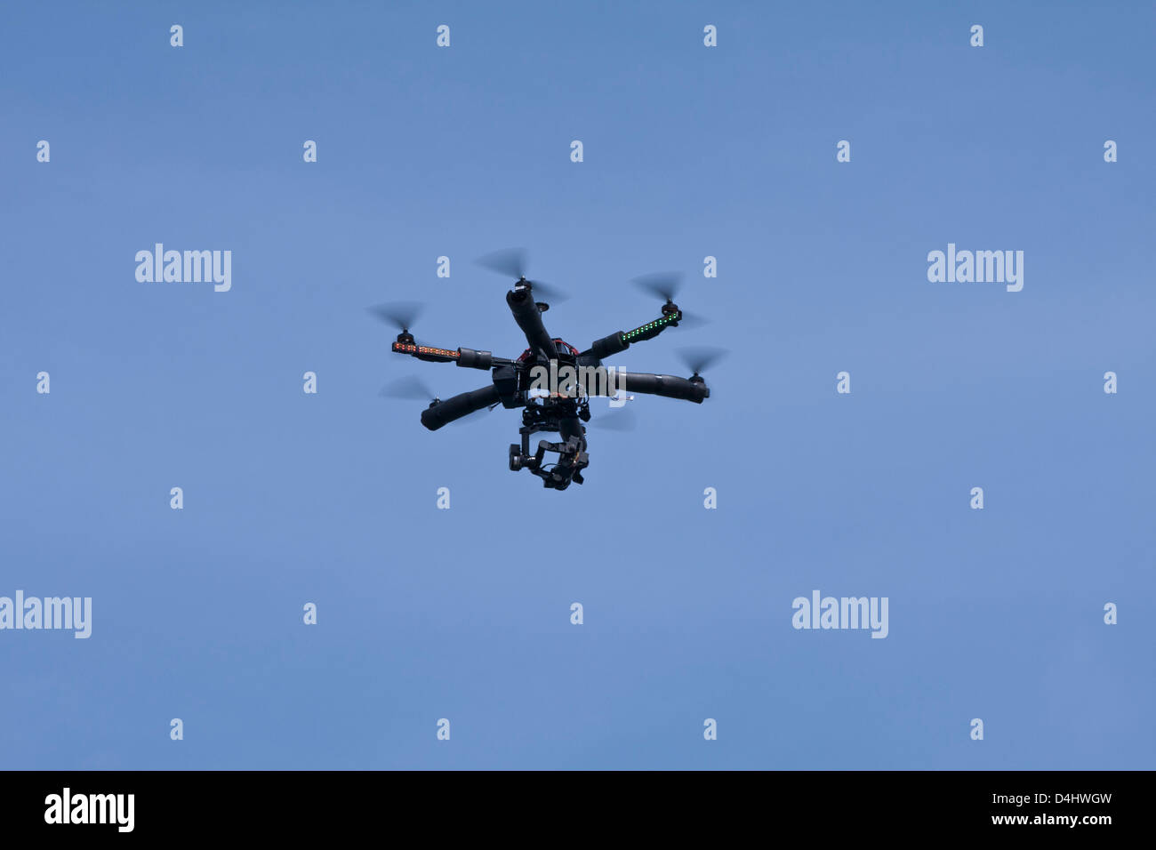 Remote radio controlled helicopter with a small video camera flies against a blue sky. Stock Photo