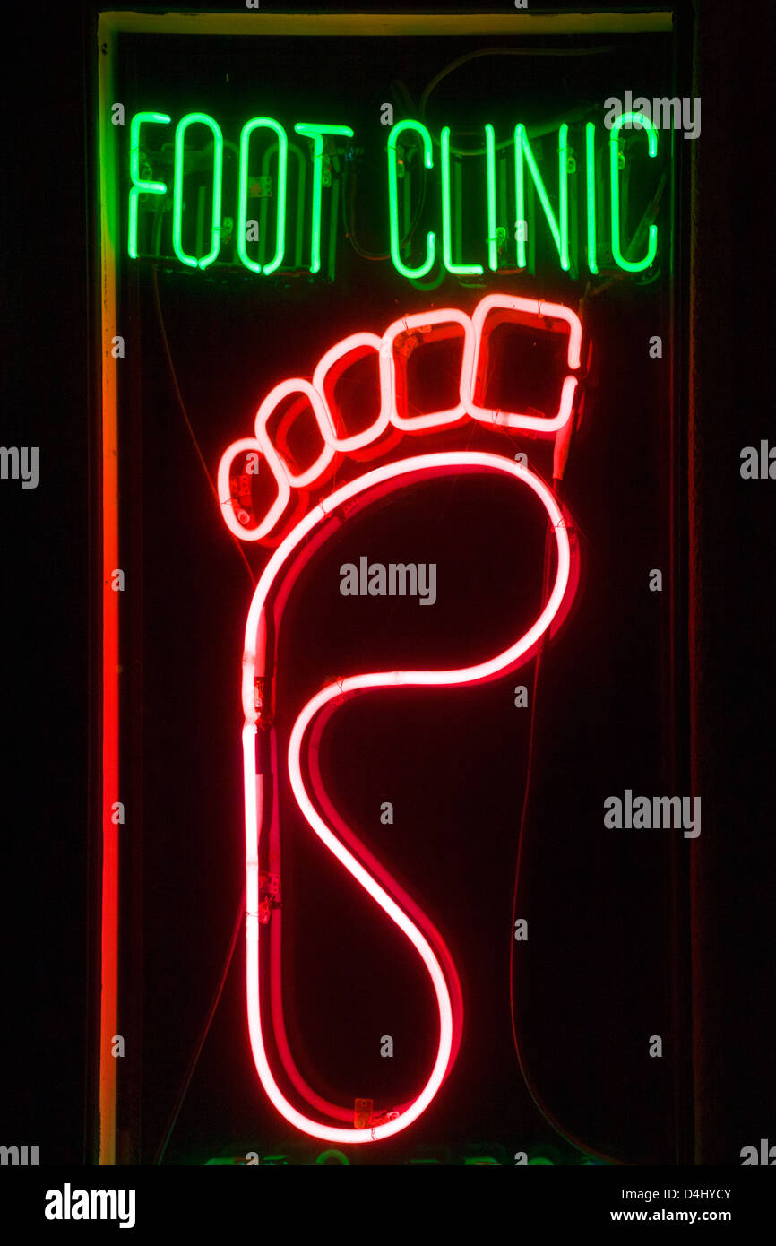 A stylized neon sign caricature of a foot advertises a storefront medical clinic at night in Santa Ana, CA. Stock Photo