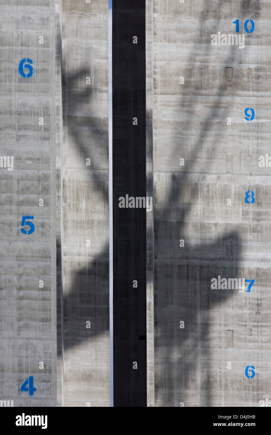 The shadow of a crane is spread across the concrete surface of a lift shaft with their floors marked vertically at 5 Broadgate, designed by Make Architects which will become the new home of UBS in London when fully occupied. Rising towards the sky is the tower-like structure with blue numbers of future storeys, stencilled on to the grey reinforced concrete. Stock Photo