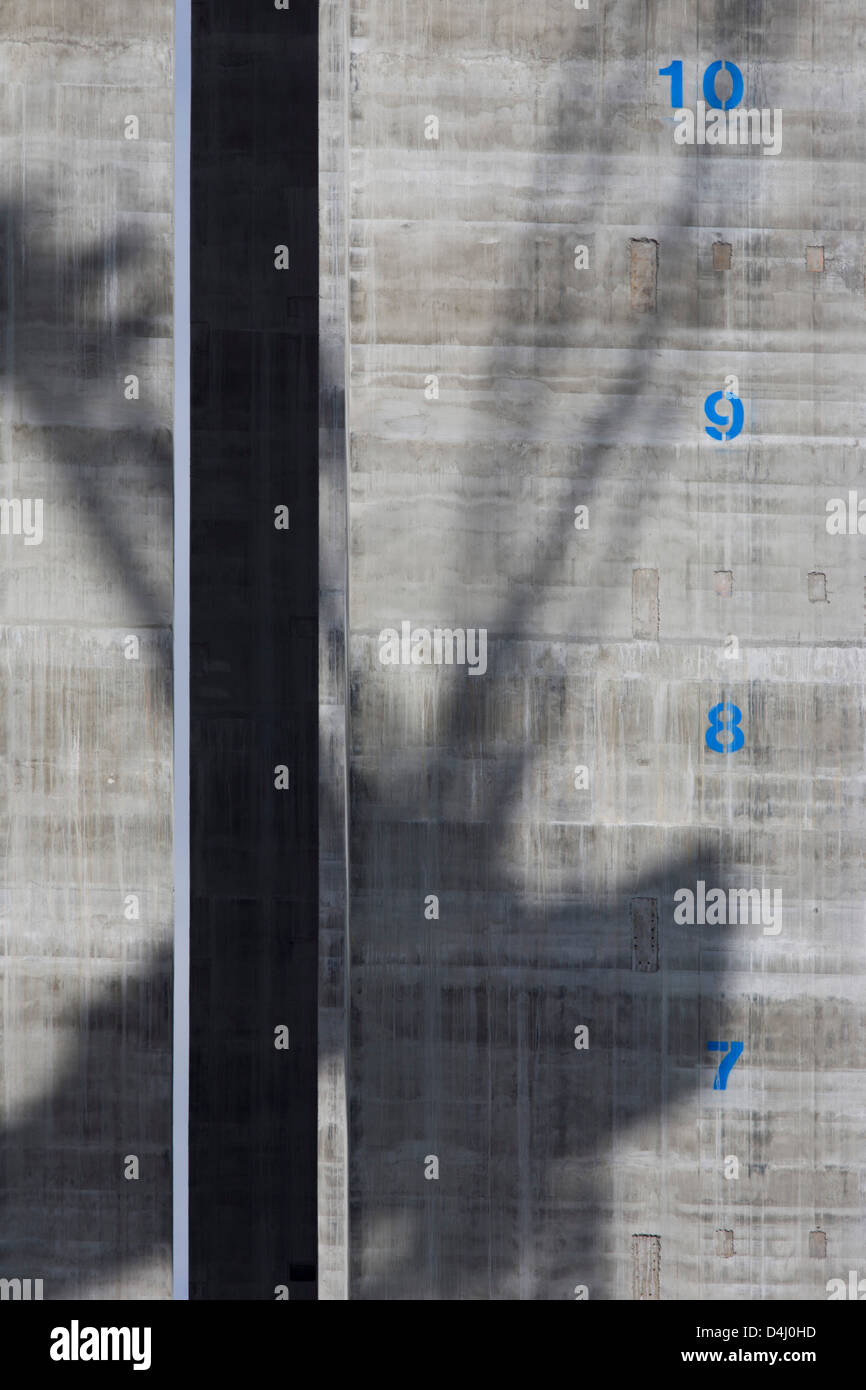 The shadow of a crane is spread across the concrete surface of a lift shaft with their floors marked vertically at 5 Broadgate, designed by Make Architects which will become the new home of UBS in London when fully occupied. Rising towards the sky is the tower-like structure with blue numbers of future storeys, stencilled on to the grey reinforced concrete. Stock Photo