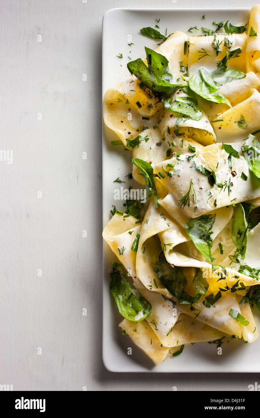 A plate of pappardelle pasta with creamy ricotta, baby spinach, fresh herbs and black pepper. Stock Photo