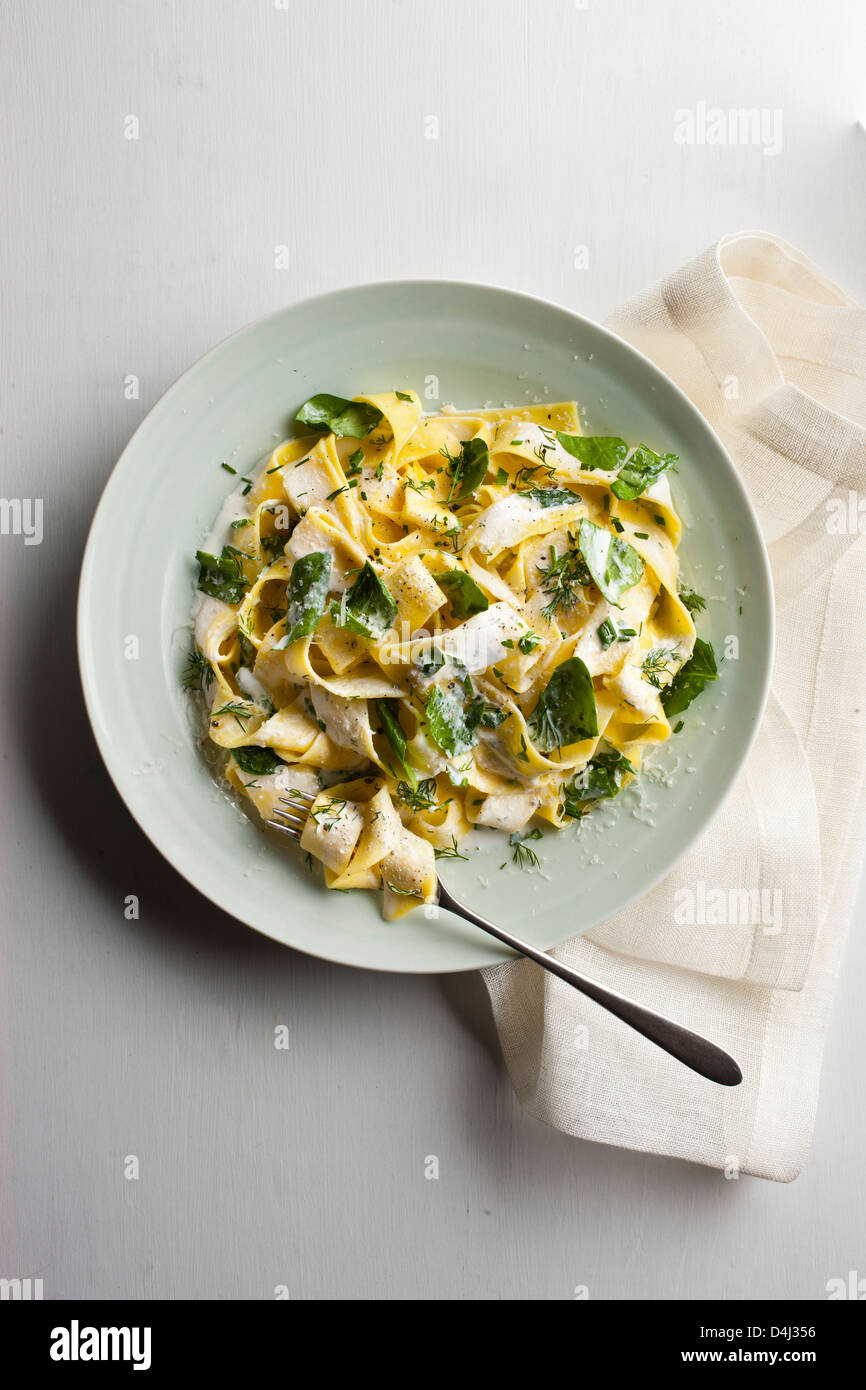 A plate of pappardelle pasta with creamy ricotta, baby spinach, fresh herbs and black pepper. Stock Photo