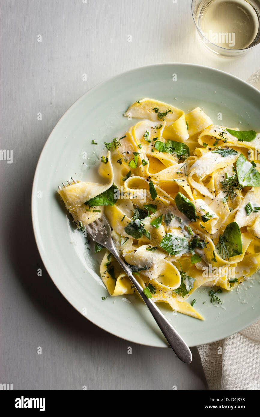 A plate of pappardelle pasta with creamy ricotta, baby spinach, fresh herbs and black pepper. Stock Photo