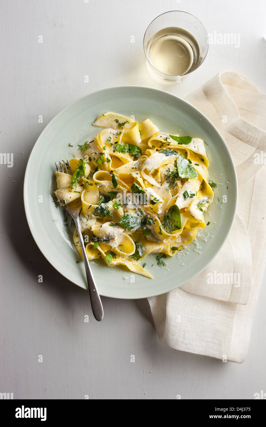 A plate of pappardelle pasta with creamy ricotta, baby spinach, fresh herbs and black pepper. Stock Photo