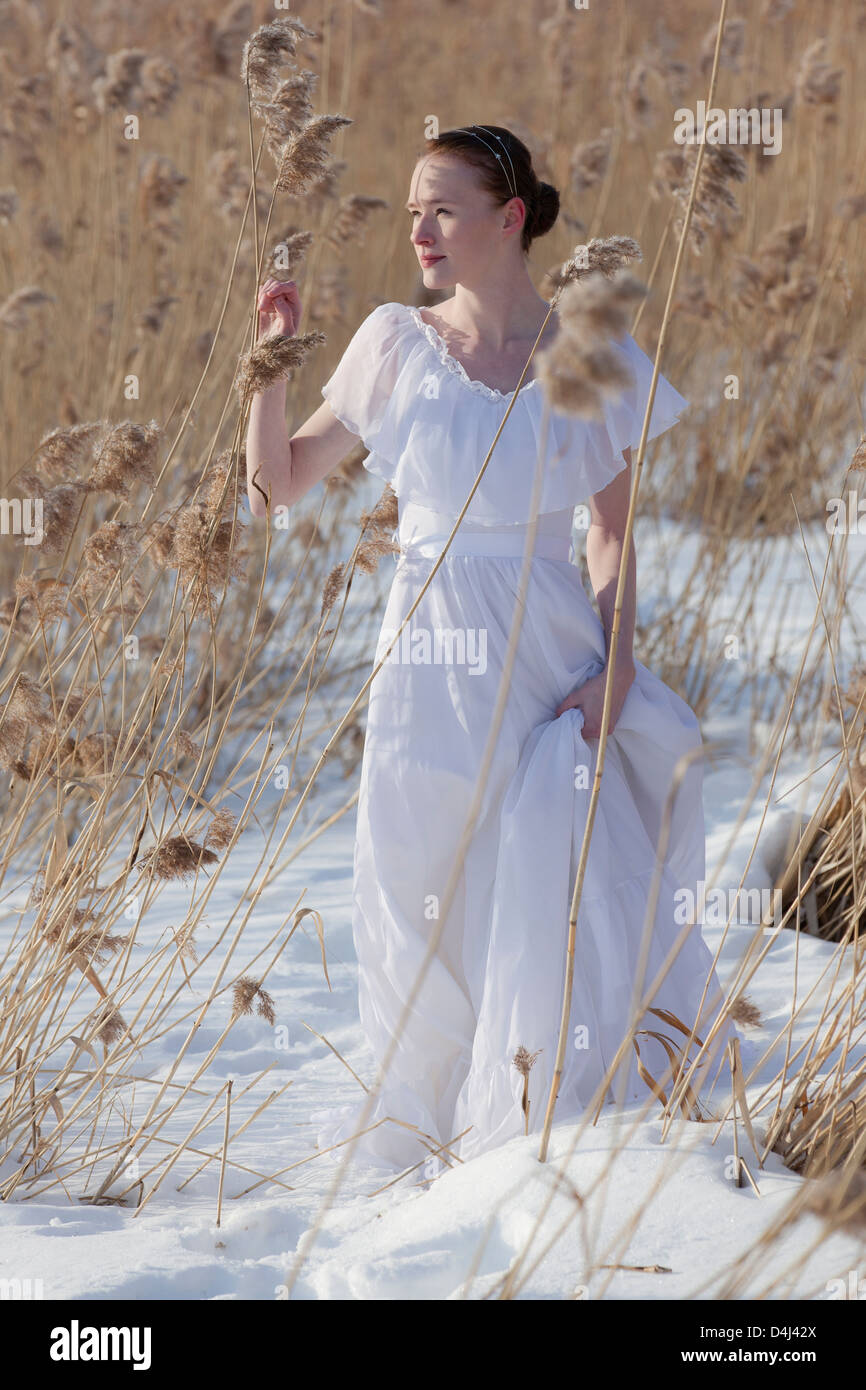 The young bride wearing wedding dress on the ice and snow in the wintertime when the sun is shining. Stock Photo