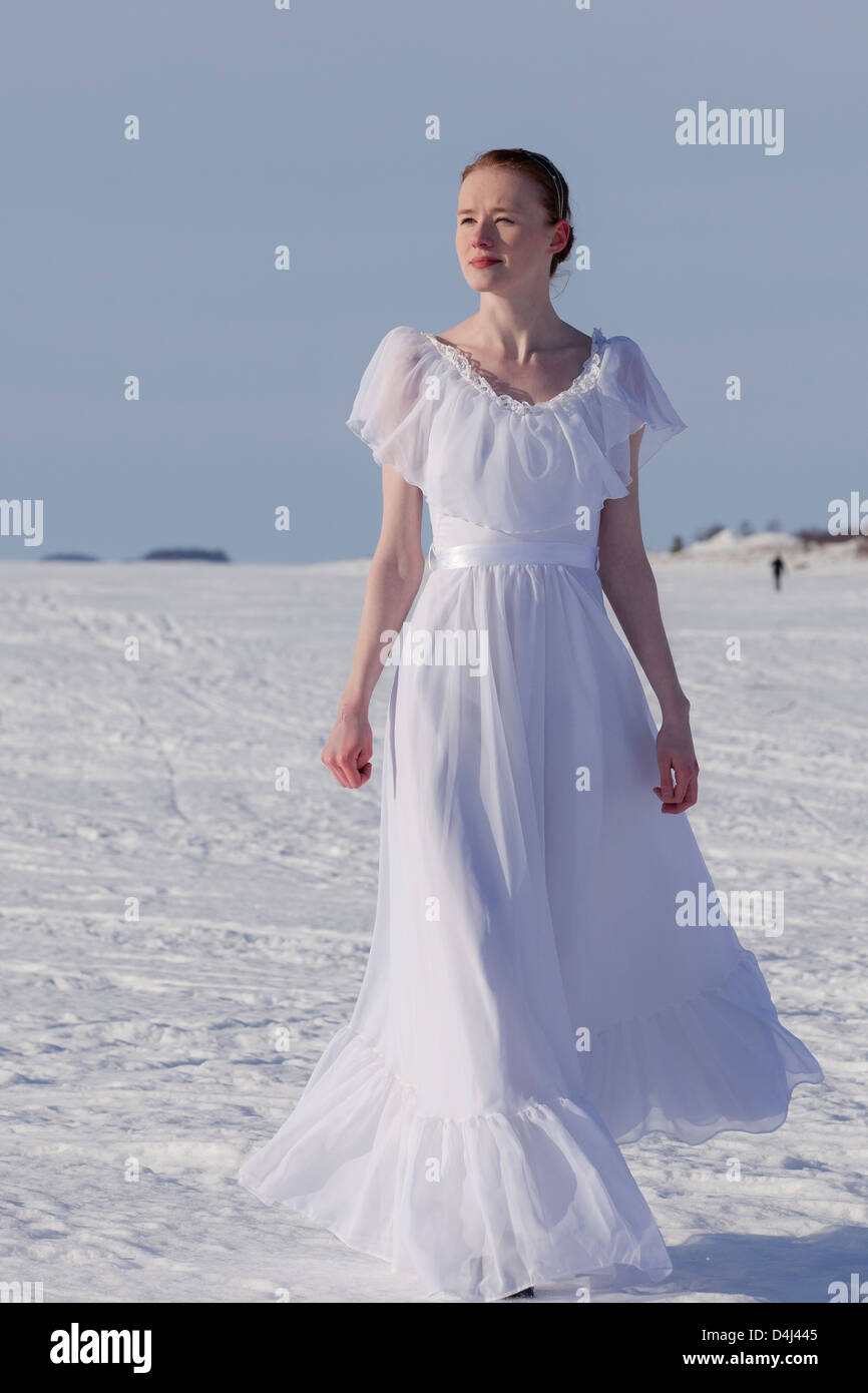 The young bride wearing wedding dress on the ice and snow in the wintertime when the sun is shining. Stock Photo