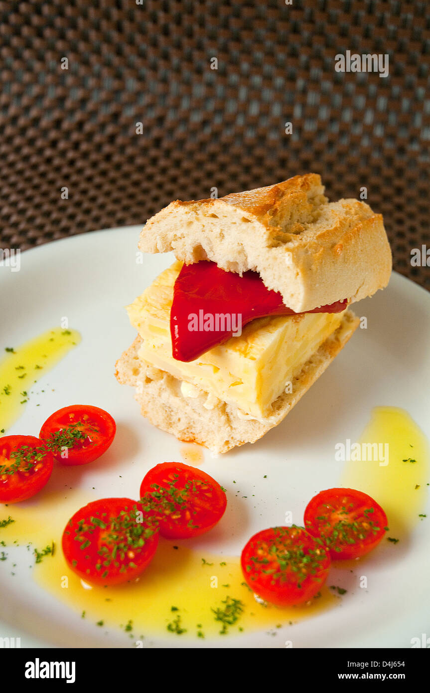 Spanish tapa: sandwich of Spanish omelet with Piquillo pepper, olive oil and cherry tomatoes. Close view. Stock Photo
