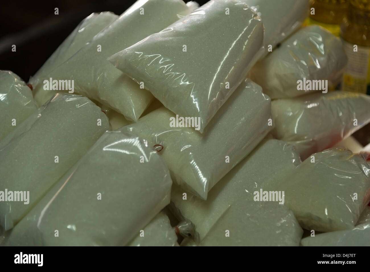 Clear plastic bags of sugar sit in a pile on a table in a market Stock